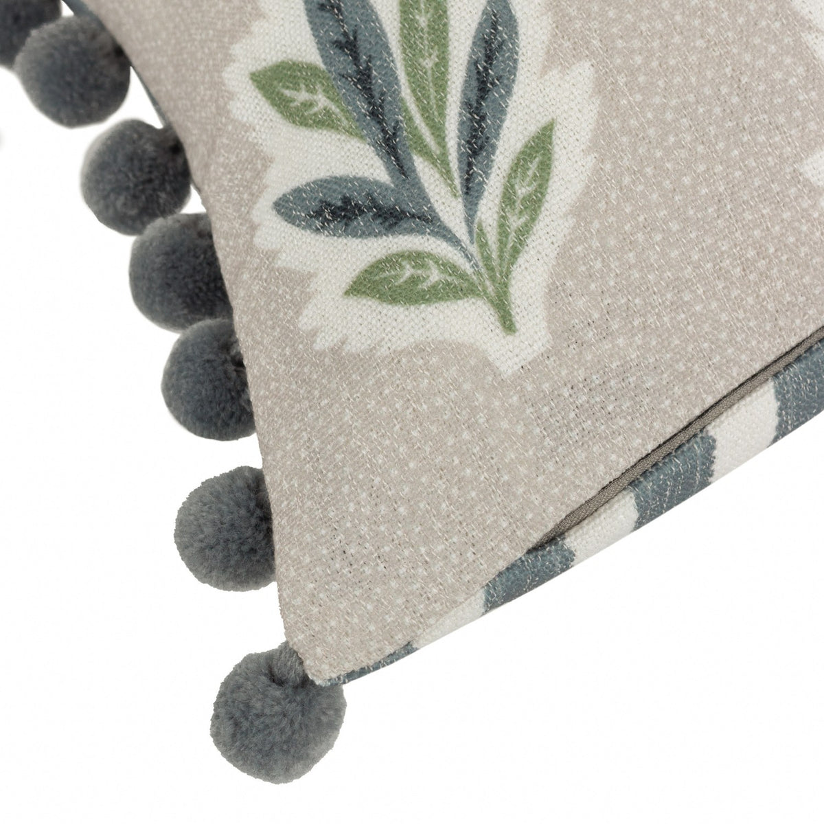 Close-up of the Sessile Leaf Reversible Cotton Cushion in Flax, showing green and slate blue leaf sprigs on a flecked beige cotton ground with a grey pom-pom trimmed edge.