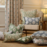Sessile Leaf reversible cotton cushions in green and slate blue leaf print styled with matching curtains and pillows on an armchair in a living room setting.