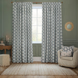 Sessile Leaf pencil pleat curtains in Delph Blue with a repeating white leaf motif, shown as a lined polyester pair framing a window in a sage-green living room.