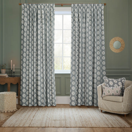 Sessile Leaf pencil pleat curtains in Delph Blue with a repeating white leaf motif, shown as a lined polyester pair framing a window in a sage-green living room.