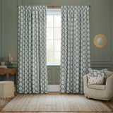 Sessile Leaf pencil pleat curtains in Delph Blue with white oak leaf motif, shown pair hanging in a green-walled living room beside a striped armchair.