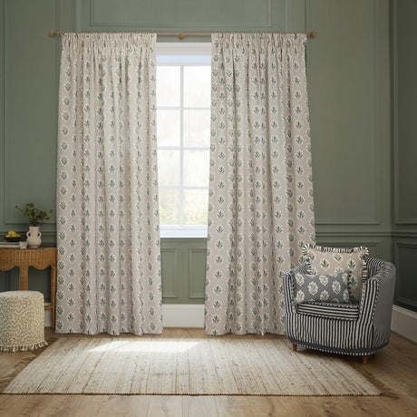 Sessile Leaf pencil pleat curtains in flax-beige polyester with green and slate blue leaf print, shown pencil-pleated on a wooden pole in a green-panelled living room.