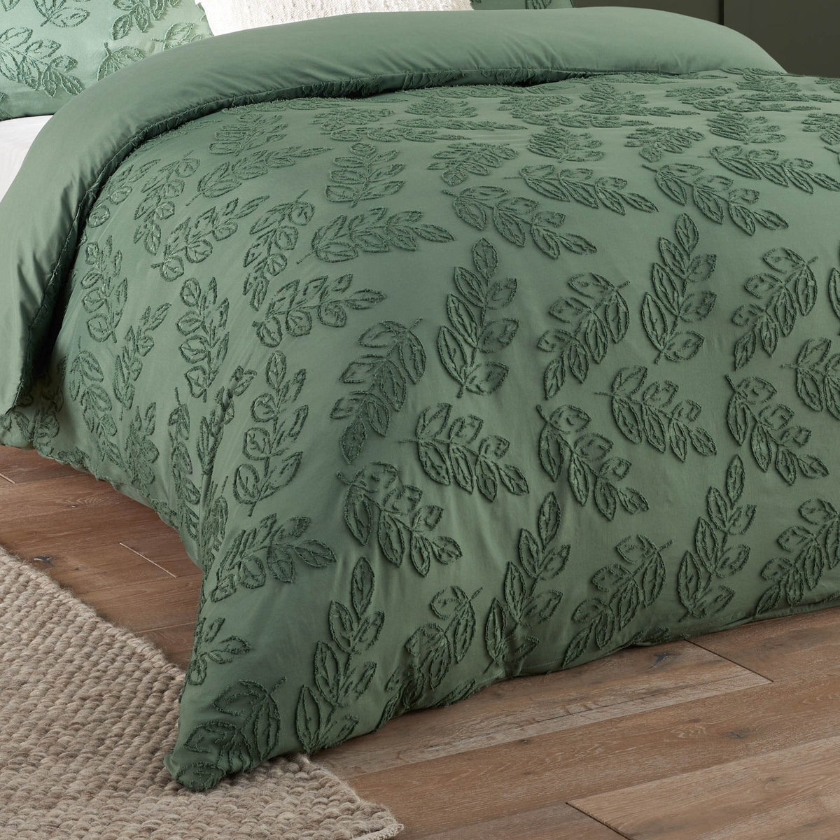 Seville Leaf Tufted Floral Duvet Cover Set in green, showing tonal chenille-style leaf pattern on a plain duvet, styled on a bed with wooden flooring.