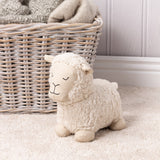 Sheep Wool Cotton Door Stop in white, with curly sherpa body and woven herringbone face, ears and feet, shown on cream carpet beside a wicker basket.
