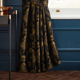 Shiraz Jacquard Chenille pencil pleat curtain in black with gold floral damask pattern, shown pleated against a dark blue panelled wall in a living room setting.