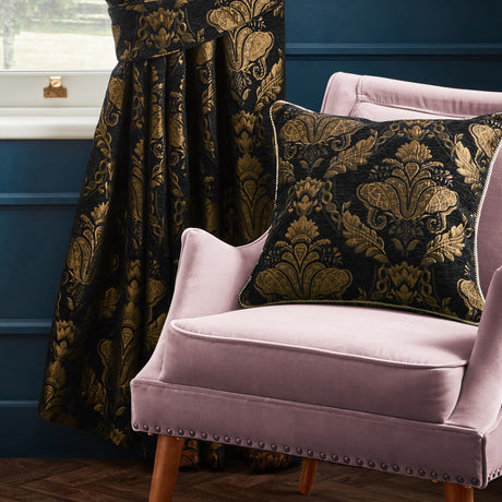 Shiraz Jacquard Chenille Cushion in black with gold floral damask pattern and corded edge, shown on a pink velvet armchair beside matching curtains.