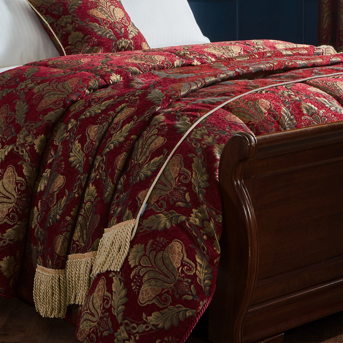 Shiraz Jacquard Chenille Throw in burgundy red with gold floral damask pattern and twisted gold fringe edging, draped over a bed with matching cushion shams.