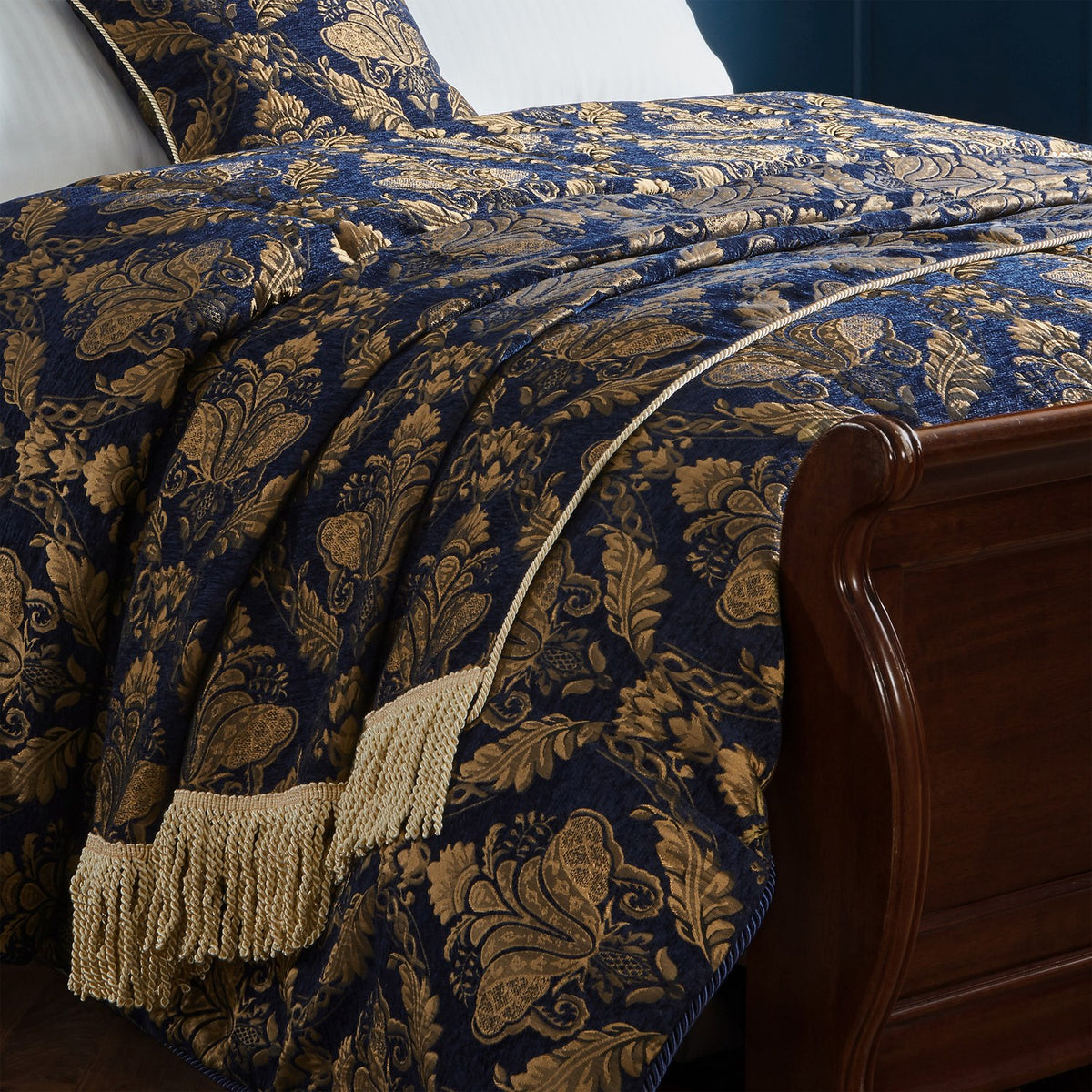 Shiraz Polyester Throw in navy with gold damask jacquard pattern, tasselled fringe edge, draped over a bed beside a dark wood sleigh frame.