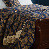 Shiraz Polyester Throw in navy with gold damask jacquard pattern, tasselled fringe edge, draped over a bed beside a dark wood sleigh frame.
