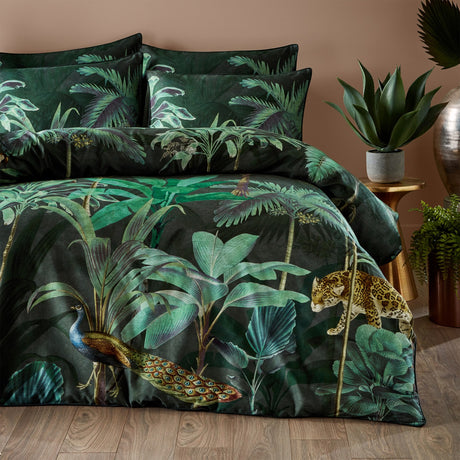 Siona Cotton Jungle Duvet Cover Set in green multicolour, printed with peacock, leopard and palm foliage on a dark ground, shown with matching pillowcases on a bed.