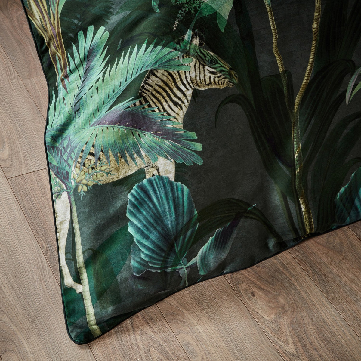 Siona Cotton Jungle Duvet Cover corner, dark green cotton fabric printed with palm leaves and a zebra, shown angled on a wooden floor.