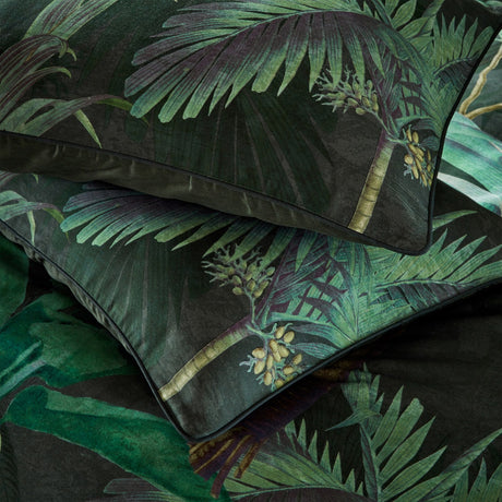 Siona Jungle Cotton Pillowcase Pair in Multi, shown stacked with a dense tropical palm print in green tones and amber-gold fruit clusters on a near-black ground, finished with a plain trim edge.