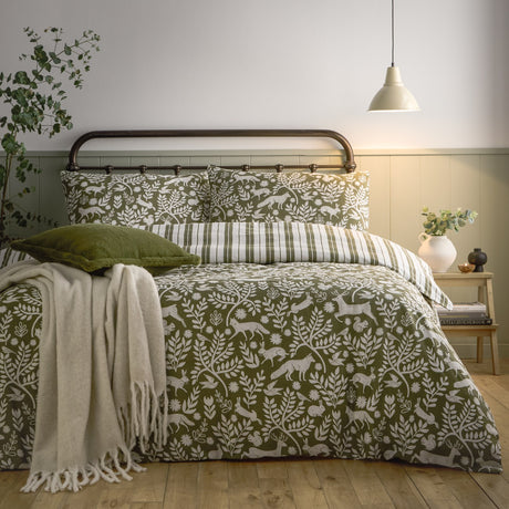 Skandi Woodland Cotton Animal Duvet Cover Set in Thyme Green on a bed, showing the green woodland print with cream fox, hare and deer silhouettes alongside striped pillowcases in a bedroom setting.