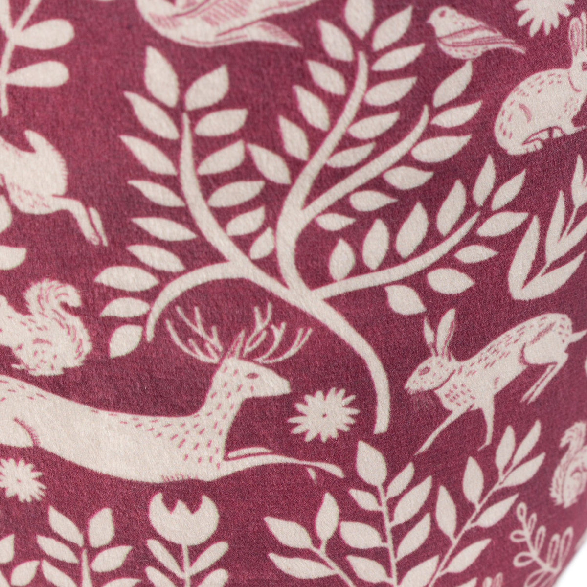 Close-up of the Skandi Woodland Animal Velvet Door Stop in berry, showing cream folk-art print of hares, a leaping stag, squirrels and birds among leafy branches on soft velvet.