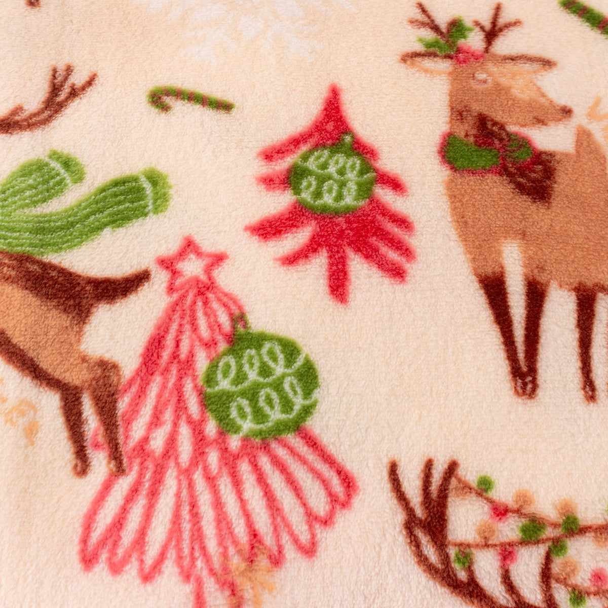 Close-up of the Sleigh Team Printed Polyester Throw in cream, showing brown reindeer, pink and red Christmas trees with green baubles, and candy canes on soft fleece fabric.