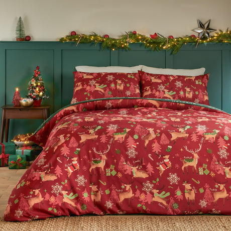 Red reversible duvet cover set with printed reindeer, Christmas trees, snowflakes and candy canes, styled on a bed with matching pillowcases in a festive bedroom setting.