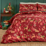 Sleigh Team Printed Reversible Duvet Cover Set in red, styled on a bed with matching pillowcases featuring reindeer, trees, and snowflakes, in a bedroom setting with festive decor.