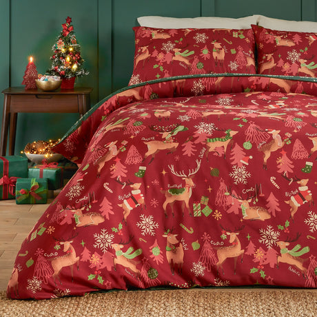 Sleigh Team Printed Reversible Duvet Cover Set in red, styled on a bed with matching pillowcases featuring reindeer, trees, and snowflakes, in a bedroom setting with festive decor.
