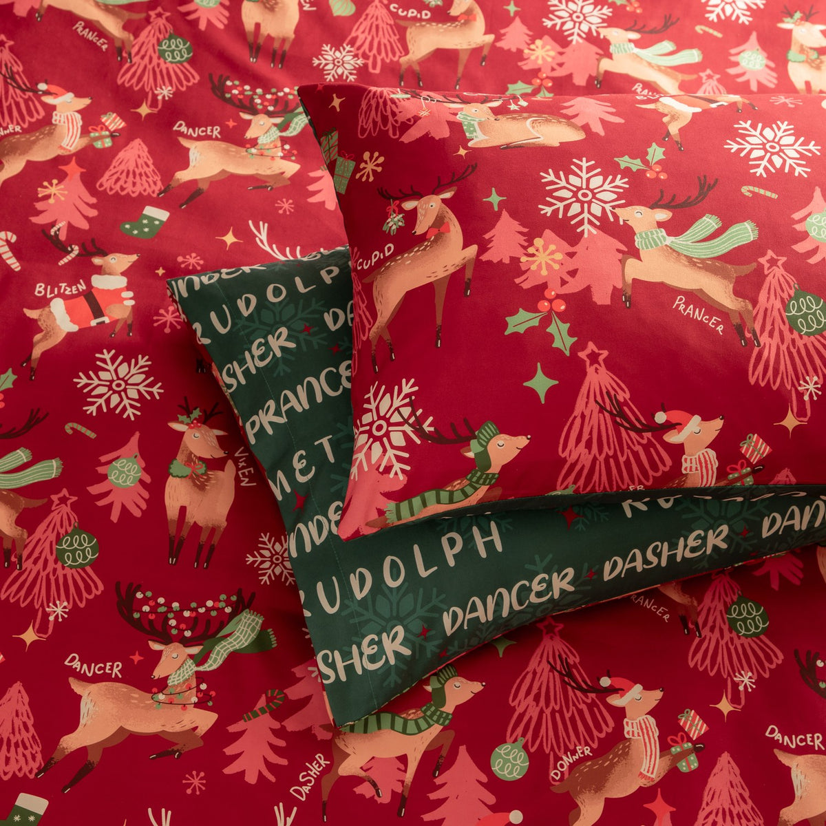Sleigh Team reversible duvet cover set in red, printed with reindeer, Christmas trees and snowflakes, folded back to show the green reverse side with reindeer names.