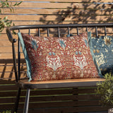 Rectangular Snakeshead Floral polyester cushion in berry red with tan, cream and teal floral pattern and sage-green Oxford trim, shown on an outdoor bench.
