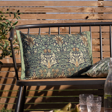 Rectangular Snakeshead Floral polyester cushion in indigo with leaf-green foliage and cream and gold blooms, shown on an outdoor bench with green piped edging.