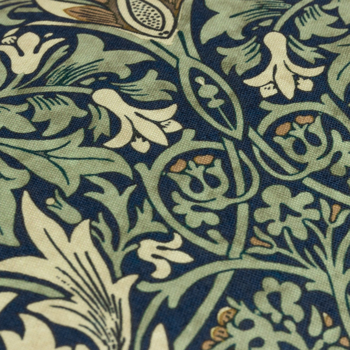 Close-up of the Snakeshead Floral polyester cushion fabric in indigo, showing leaf-green foliage and cream and gold botanical blooms in a traditional Morris & Co. print.