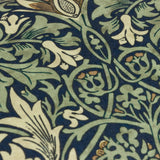 Close-up of the Snakeshead Floral polyester cushion fabric in indigo, showing leaf-green foliage and cream and gold botanical blooms in a traditional Morris & Co. print.