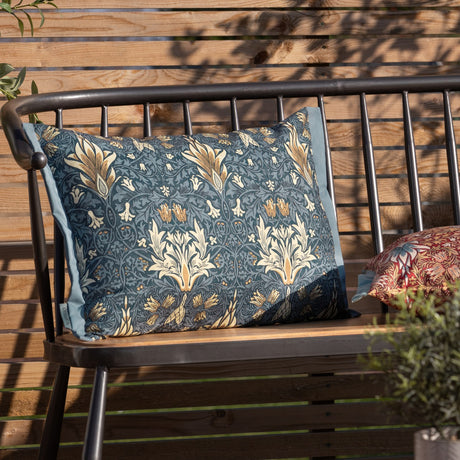 Rectangular Snakeshead Floral polyester cushion in indigo with cream and gold floral print, shown on a metal-framed bench with wooden slats in an outdoor setting.