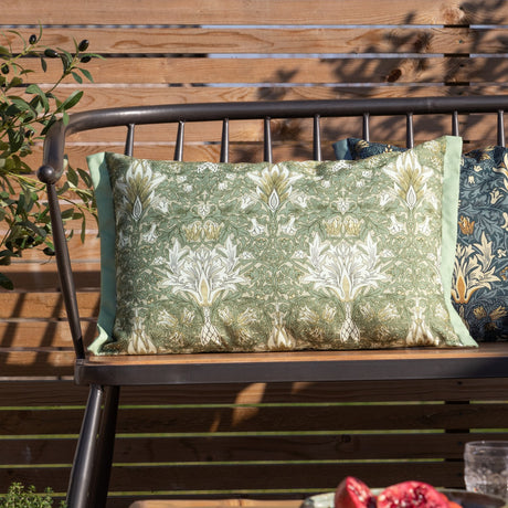 Rectangular Snakeshead Floral polyester cushion in green, gold and cream on a stone ground, with mint piped edges, shown on an outdoor bench.
