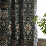 Pencil pleat curtains in Snakeshead jacquard chenille, Indigo/Leaf, showing folded fabric with floral and foliage pattern near a window with greenery.