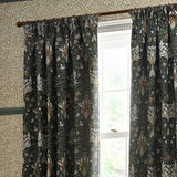 Snakeshead Jacquard Chenille pencil pleat curtains in Indigo/Leaf, floral fritillary pattern in navy, green and cream, shown pleated on a wooden pole beside a window.