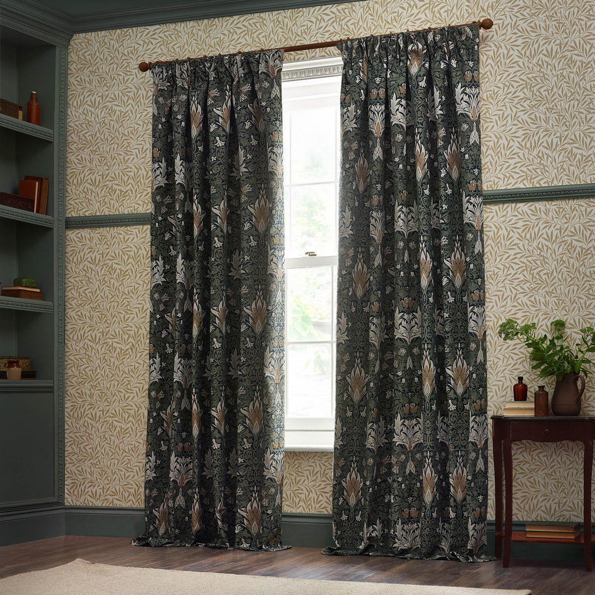 Pencil pleat curtains in Snakeshead jacquard chenille, Indigo/Leaf colourway, hung either side of a window in a traditional study with panelled walls and shelving.