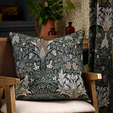 Snakes Head jacquard chenille cushion in indigo and leaf green, floral William Morris pattern, styled on a wooden armchair in a living room setting.