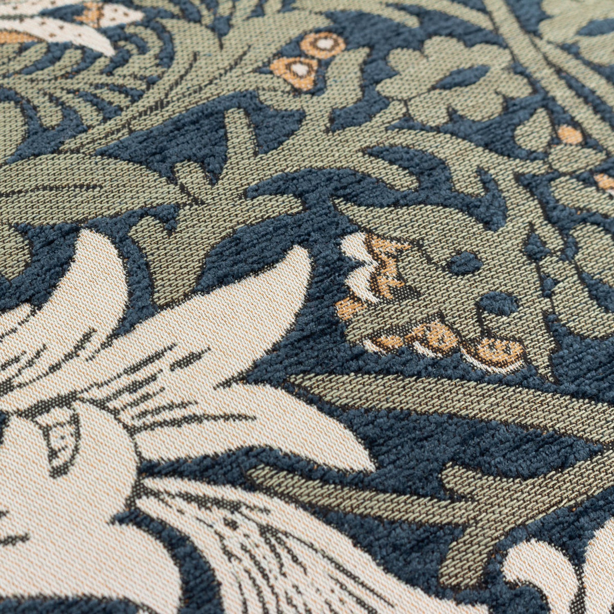 Close-up of the Snakes Head jacquard chenille cushion showing raised floral and foliage patterning in indigo, leaf green, cream and tan tones.