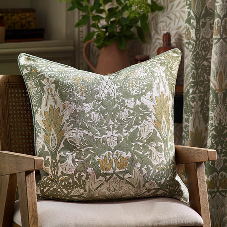 Snakes Head Jacquard Chenille Cushion in Sunflower/Stone, sage green ground with cream foliage and gold flowerheads, shown on a wooden armchair in a living room setting.