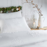 White Snow Crystal duvet cover set with raised tufted snowflake motifs on pillows and bedding, shown on a bed in a bedroom setting with candles and greenery.