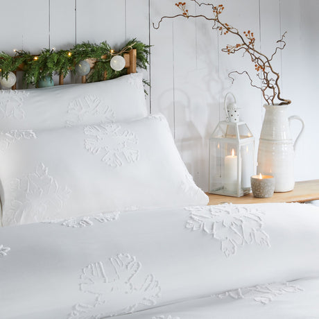 White Snow Crystal duvet cover set with raised tufted snowflake motifs on pillows and bedding, shown on a bed in a bedroom setting with candles and greenery.
