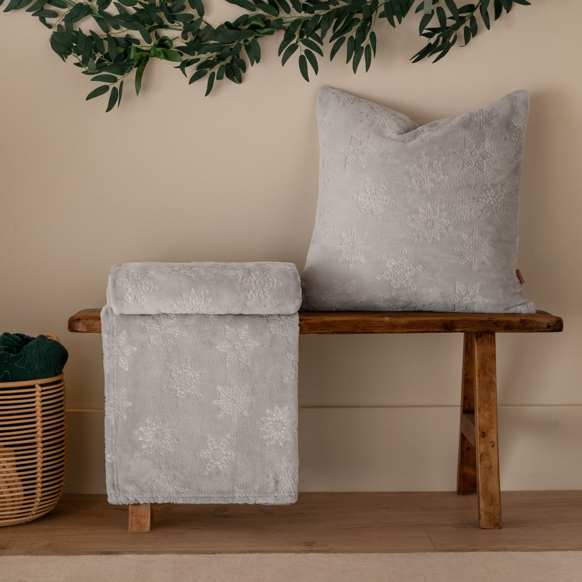Grey faux fur throw with embossed snowflake pattern draped over a wooden bench beside a matching snowflake-textured cushion, in a living room setting.