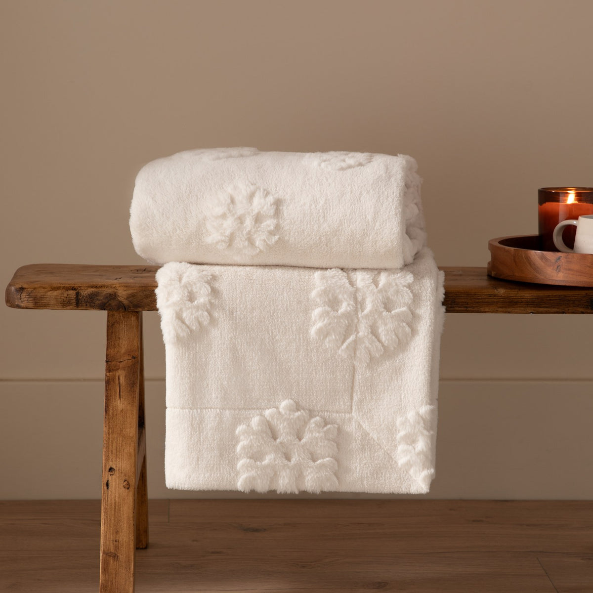 Snowflakes Faux Fur Polyester Velvet Throw in snow white, folded and draped over a wooden bench, showing raised snowflake motifs on a soft, deep-piled surface.