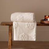 Snowflakes Faux Fur Polyester Velvet Throw in snow white, folded and draped over a wooden bench, showing raised snowflake motifs on a soft, deep-piled surface.