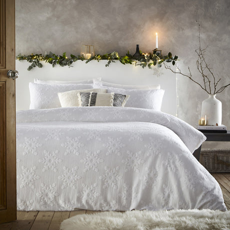 White cotton duvet cover set with tufted snowflake pattern, styled on a bed with matching pillow shams in a softly lit bedroom.