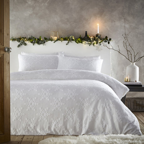 White cotton duvet cover set with tufted snowflake pattern and matching pillowcases, styled on a bed in a bedroom with festive greenery and candles.