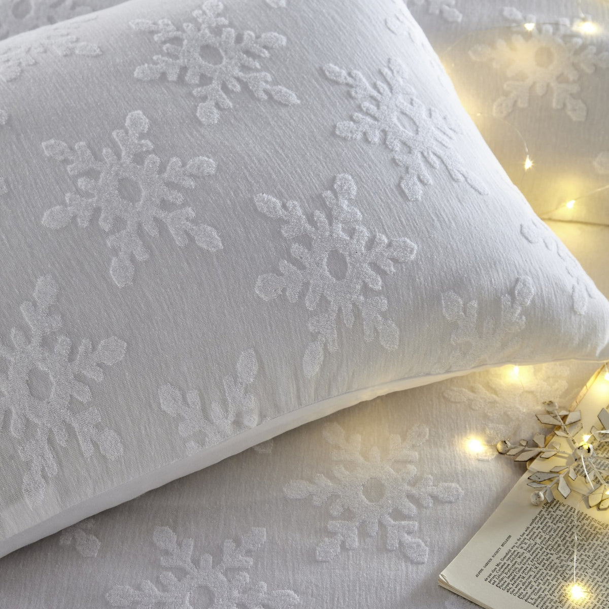 Close-up of the Snowflake Cotton Abstract Duvet Cover Set in white, showing tufted snowflake texture on a pillow, styled with fairy lights on the bed.