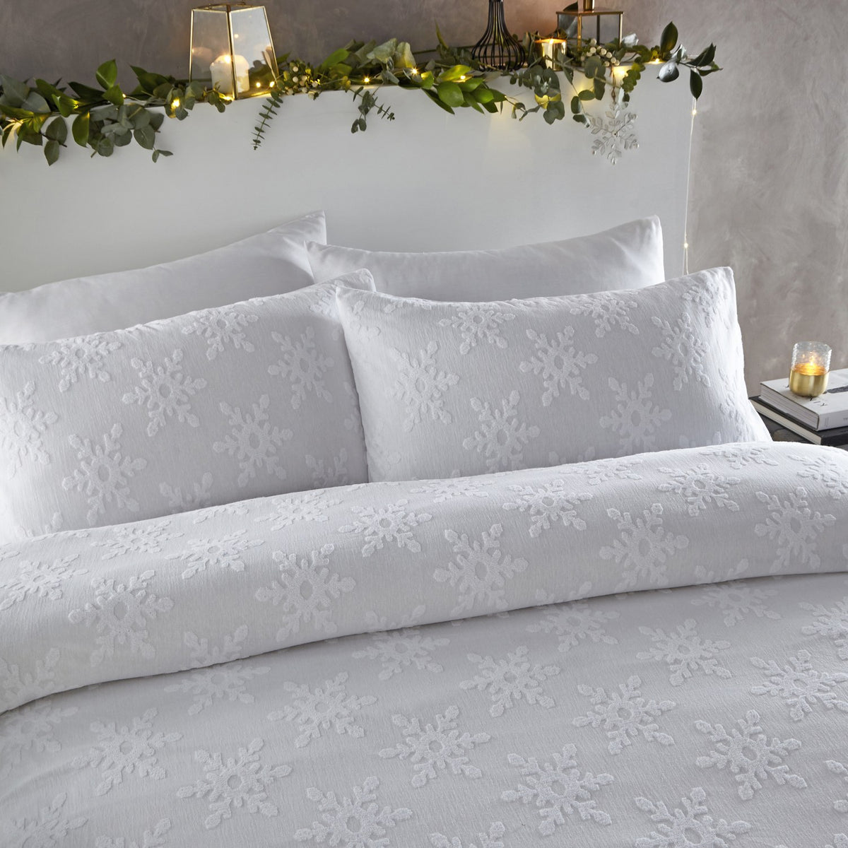 White cotton duvet cover set with tufted snowflake pattern, styled on a bed with matching pillowcases in a bedroom with festive greenery on the headboard.