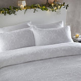 White cotton duvet cover set with tufted snowflake pattern, styled on a bed with matching pillowcases in a bedroom with festive greenery on the headboard.