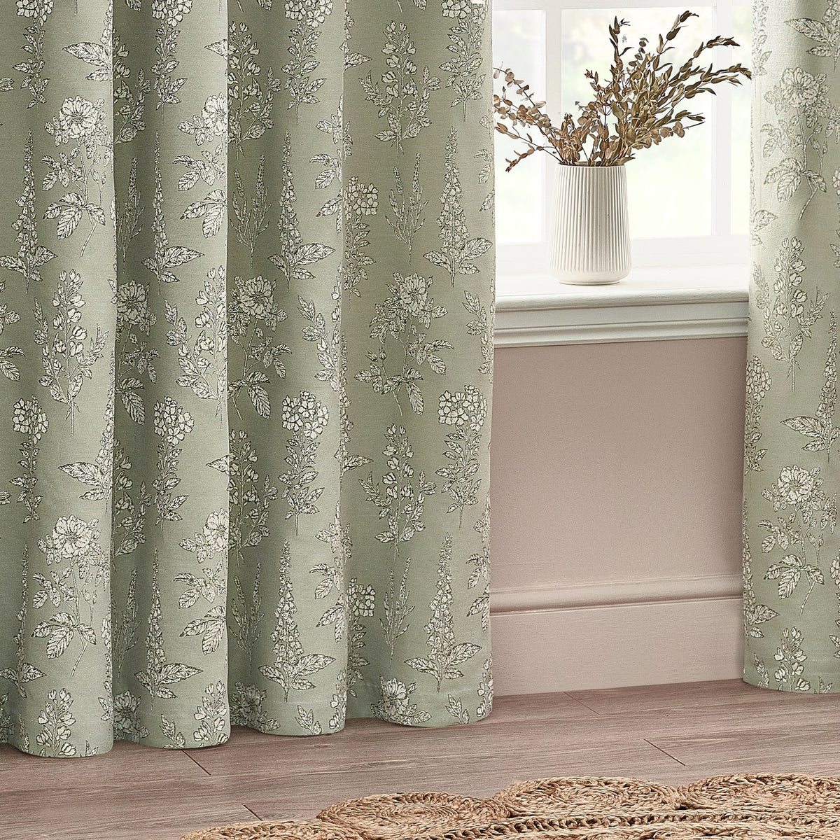 Sophia Jacquard Embroidered Eyelet Curtains in sage green with botanical floral pattern, shown framing a window beside a white vase in a living room setting.