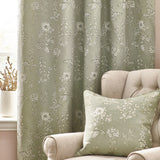 Sophia Jacquard Embroidered Eyelet Curtains in sage green with botanical foxglove and rose pattern, shown in a living room beside a matching cushion on a beige armchair.