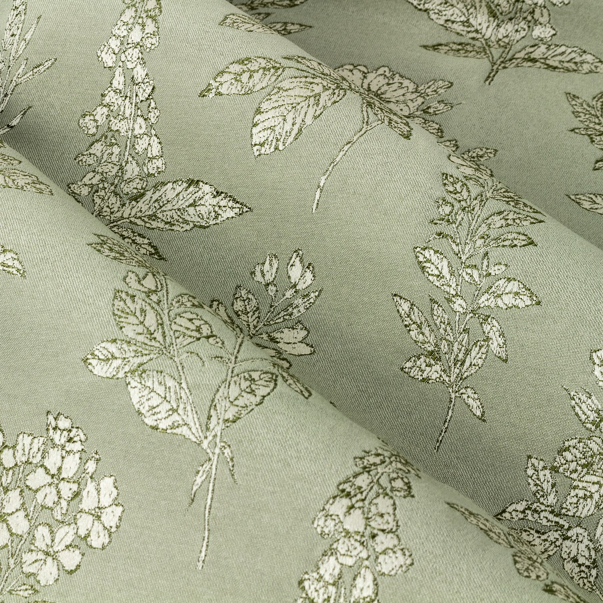Close-up of Sophia Jacquard Embroidered Eyelet Curtains in sage green, showing woven botanical pattern of foxgloves, roses and leaves on folded polyester fabric.