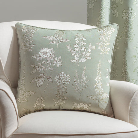 Sophia Eyelet Polyester Cushion in Sage, a 50 x 50cm square jacquard cushion with woven botanical florals and leaves in cream and olive, shown on a cream armchair.
