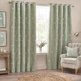 Sophia Eyelet Polyester Cushion in sage with a jacquard floral pattern, shown on a matching armchair in a living room styled with sage curtains.